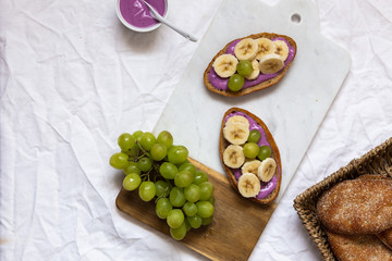 bread dessert sandwiches with yogurt and banana on a rustic cutting board with grapes on white background, top view. Flat lay. Delicious breakfast or snack