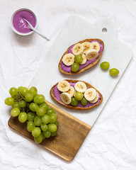 bread dessert sandwiches with yogurt and banana on a rustic cutting board with grapes on white background, top view. Flat lay. Delicious breakfast or snack