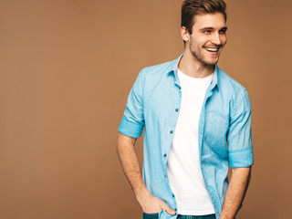 Portrait of handsome smiling stylish hipster lumbersexual businessman model dressed in blue shirt clothes. Fashion man posing on golden background