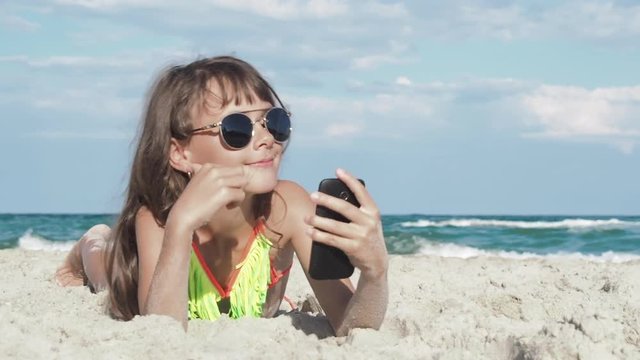 Child doing selfie on beach. Little girl is lying on the sand on the beach and is photographed on a smartphone.