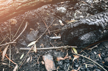 White cigarette lying on the dark black fireplace outdoors in forest. Harmful habit for health and pollution of the environment.