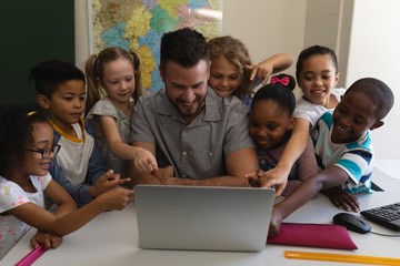Male school teacher teaching schoolkid on laptop at desk in
