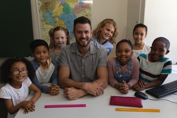 Happy male teacher and schoolkids looking at camera in classroom