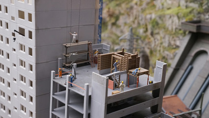 Construction site of new house with apartments with working lifting crane, new many-storied building, foreman with workers in the process, miniature