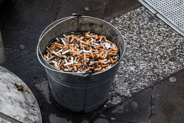 A picture of a public ashtray. The bucket with sand. Looks ugly and like a mess.