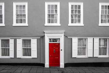 A facade of a traditional village house in Great Britain. Its red door are isolated in a black and white picture.  © shootingtheworld
