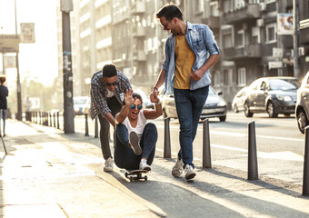 Group of friends hangout at the city street.Female sitting on skate board while friends pushing her from behind.