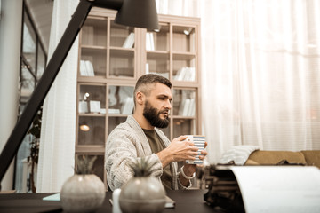 Serious thoughtful man in knitted cardigan carrying big cup of tea