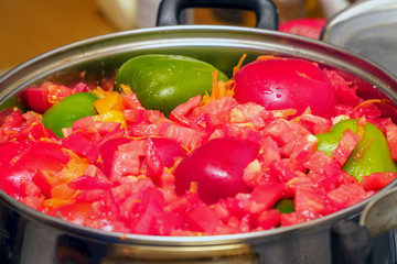 Cut into pieces vegetables - bell peppers, tomatoes, etc. - in a shiny metal pan on the kitchen table