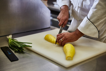 Chef slicing yellow squash on white cutting board
