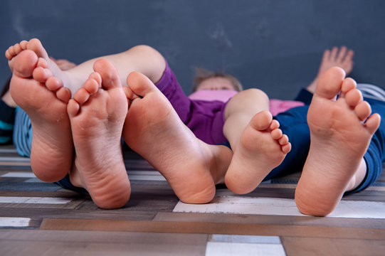 Three children are sitting on floor in room and are going to do gymnastics. Legs and feet of kids close-up. Gentle boy's skin. Beautiful shape of heels and fingers. home development of preschoolers