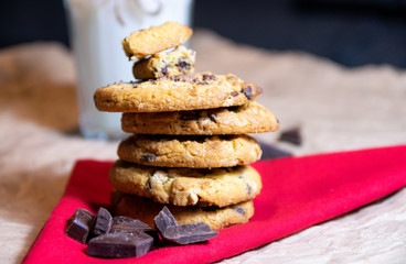 A pile of the chocolate chip cookies placed on the red cloth with a glass of milk in the background