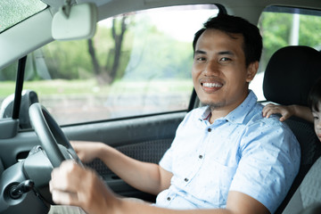 young asian driver smile to the camera when drive a car