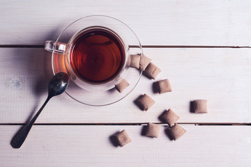 Top view of a cup of tea and sweets on a white wooden background.