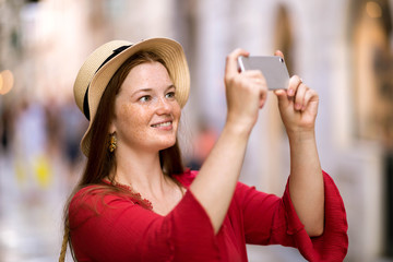 Cute girl takes pictures on a smartphone sights in travel. On the streets of a European city. Share your impressions!