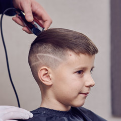 Barber making a haircut to a cute European boy using cutting machine.