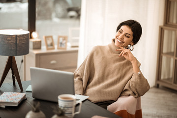 Dark-haired appealing lady sitting at the desk and watching on laptop screen