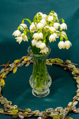 Spring flowers in a crystal vase, a circle of willow branches on a blue background