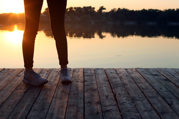 girl in sneakers on the bridge at the lake at sunset