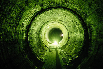 Flooded round underground drainage sewer tunnel with dirty sewage water green illuminated