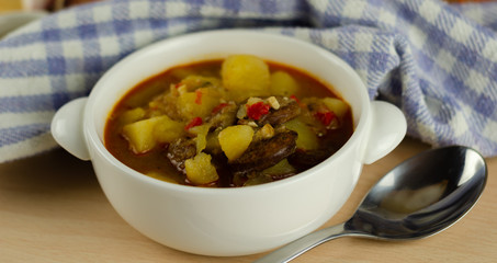 Traditional Hungarian goulash with beef, potatoes, tomatoes and peppers, a tasty dish in a white bowl