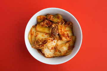 Kimchi in the white plate on the red  background.Top view.Copy space.