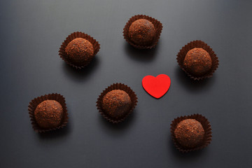 chocolate sweets in wrapper with red heart over black background