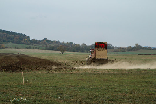 A picture of a tractor on a field during autumn. Working hard while carrying and throwing the dung on the field. 