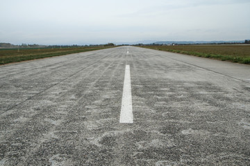 A picture of an empty long old airport runway made from conrcrete panels. 