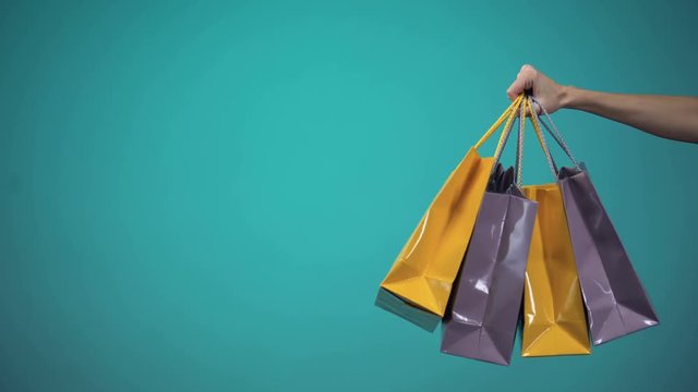 Female hand holding many colorful shopping bags on blue background, template