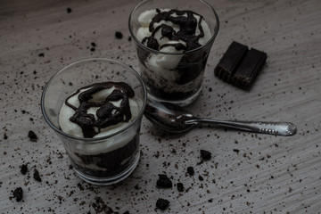 Homemade yogurt of crushed cookies, chocolate and cream with crumbs on the wooden table