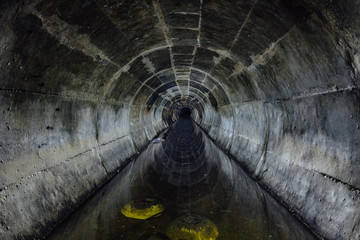 Flooded round underground drainage sewer tunnel reflecting in dirty sewage water