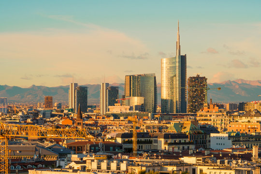 Milan (Italy) skyline at sunset with modern skyscrapers in Porta Nuova business district. Panoramic view of Milano city. The mountain range of the Lombardy Alps in the background. © Arcansél