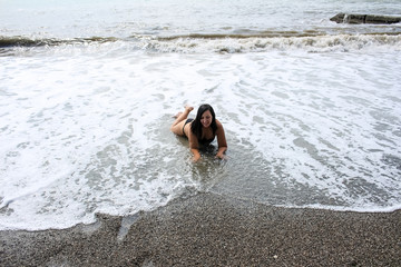 Young woman is lying on the seashore, waves and sea foam.