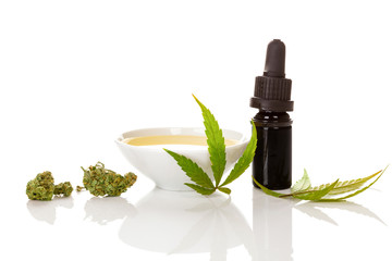 Cannabis oil in bowl with marijuana buds and leaves.