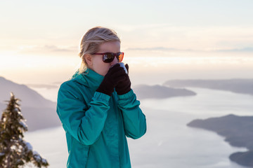 Young Caucasian Girl drinking warm beverage on top of a mountain during a beautiful winter sunset. Taken on Mnt Harvey, near Vancouver, BC, Canada.