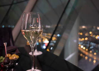 Glass of white wine on a black table in restaurant. Night city lights bokeh through panoramic windows in the background. Concept of recreation, drinking and dining in a luxury place or romantic date
