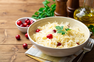 Sauerkraut with cranberries and parsley in bowl on wooden table. Selective focus.