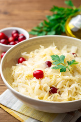 Sauerkraut with cranberries and parsley in bowl on wooden table. Selective focus.