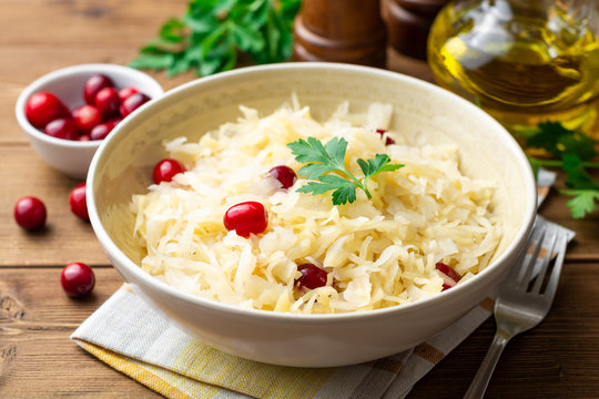 Sauerkraut with cranberries and parsley in bowl on wooden table. Selective focus.