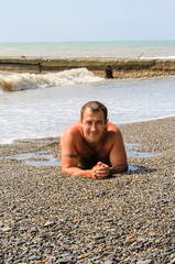 Fototapeta na wymiar A young man lies on the seashore his washes sea foam and waves