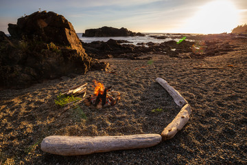 Camp fire on the beach during a vibrant summer sunset. Taken in Northern Vancouver Island Ocean Coast, BC, Canada.