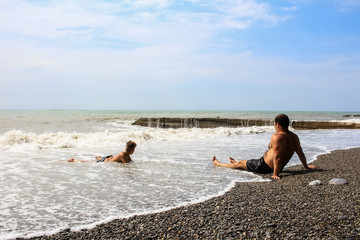 A man and a child are resting on the seashore, sea foam and waves.