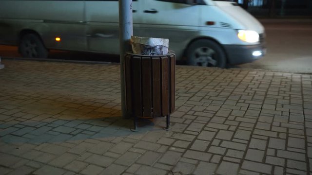 City night scene bus stop. Cat print plastic bag in sidewalk trashcan. Cat peeking out of trash can.