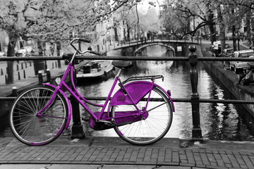 A picture of a lonely purple bike on the bridge over the channel in Amsterdam. The background is black and white. 