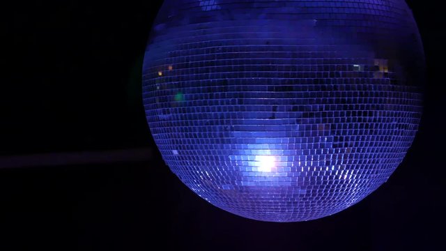 Closeup footage of a spinning mirrored sphere disco ball with reflections by colorful lights.