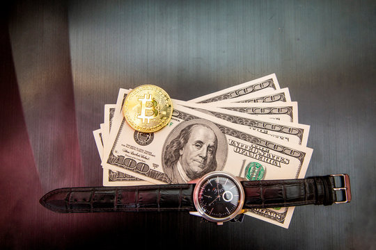 Bitcoin coin, 100 dollar bills and gold watch on dark background
