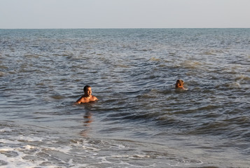 A man and a boy teenager swim in the sea, on big waves