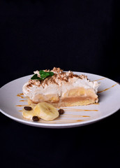 Piece of Banoffee pie on a white plate against the black background