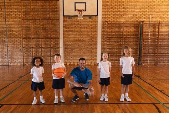 Happy basketball coach and schoolkids looking at camera at
